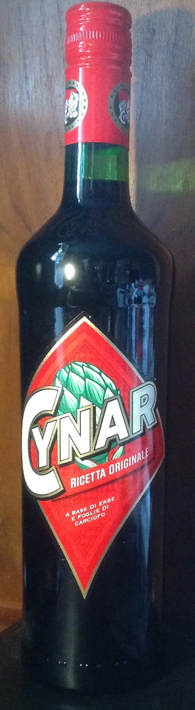 濃緑色の瓶に赤いキャップシールがかかり、赤いひし形ラベルの中央に白抜きで「CYNAR」、上部に緑色のアーティチョークのイラストが描かれている。背景は木目調