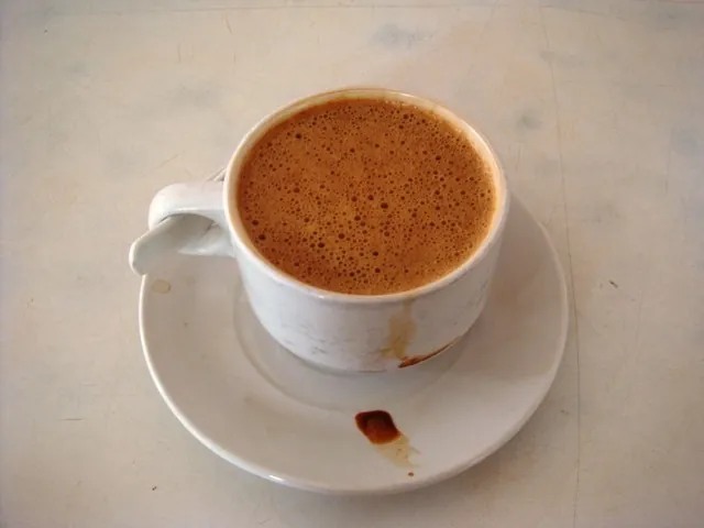 白いカップとソーサーに、薄茶色できめ細かな泡がびっしり浮いた飲料が入っている。ソーサーには数滴のこぼれ跡がある。