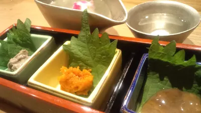 漆塗りの箱に3種の珍味が小鉢で並び、奥に酒器が置かれている