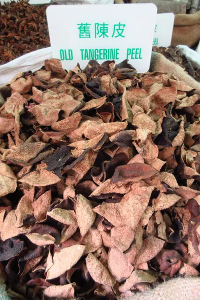 白い札に緑字で「舊陳皮 OLD TANGERINE PEEL」と書かれ、その手前に赤褐色から黒褐色まで色むらのある反り返った果皮の破片が山積みになっている。