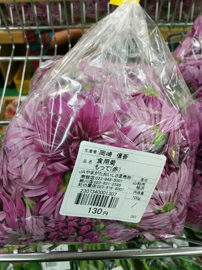 透明な袋に詰められた、赤紫色の細い花弁を密集させた食用菊の花が複数入っている。袋には生産者名・品名・産地・内容量を記した白いラベルが貼られている。