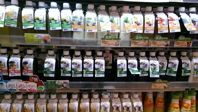 冷蔵棚に、白いキャップの付いた瓶入り飲料が数十本並び、それぞれに湯呑みに入った褐色の液体を描いたラベルが貼られている。棚の緑色の値札には「漢方涼茶」の文字がある。