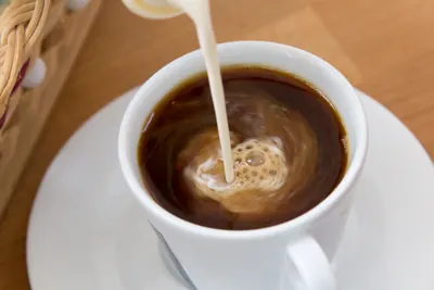 白いコンデンスミルクが黒いコーヒーの中に注がれている写真